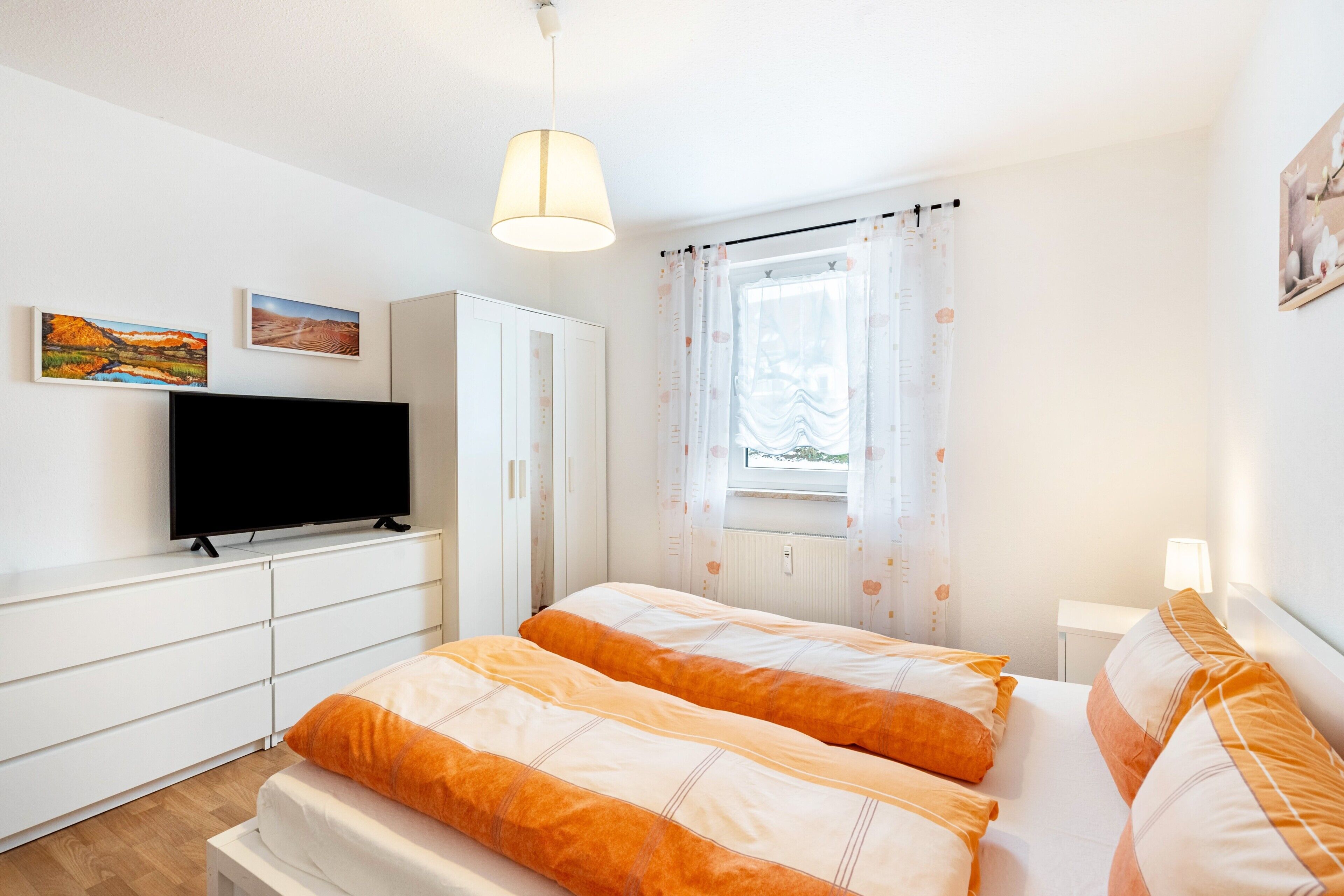 A bedroom with a bed, a TV, a wardrobe, and a window with curtains.