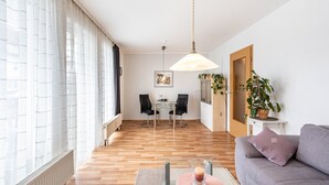 Un salon moderne avec un canapé, une table à manger et des chaises, un luminaire suspendu et une plante en pot.