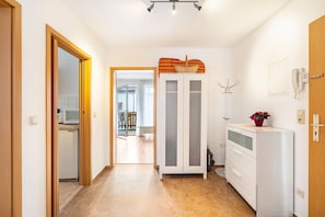 Un couloir avec un four à micro-ondes, un meuble sur lequel est posé un panier, un téléphone fixé au mur et une porte donnant sur une autre pièce.
