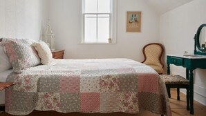 Un dormitorio con una cama, una silla, un escritorio, una ventana y un cuadro colgado en la pared.