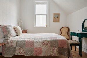 A bedroom with a bed, a chair, a desk, a window, and a wall-mounted picture.