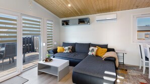 A modern living room with a sofa, a coffee table, and a TV stand. There is a sliding glass door leading to an outdoor area. - Holiday Home 'Madera Concordiasee' with Wi-Fi and Air Conditioning (Seeland)