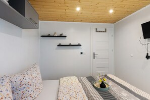 Ein Schlafzimmer mit Bett, Nachttisch mit Vase, Wand-Fernseher und Holzboden.