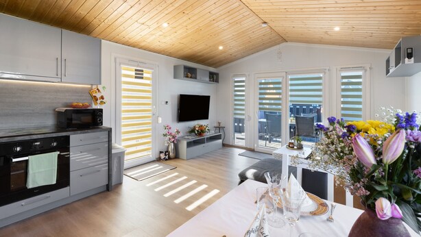 A modern kitchen with a flat-screen TV, wooden ceiling, and a dining area with a table set for two. - Holiday Home 'Madera Concordiasee' with Wi-Fi and Air Conditioning (Seeland)