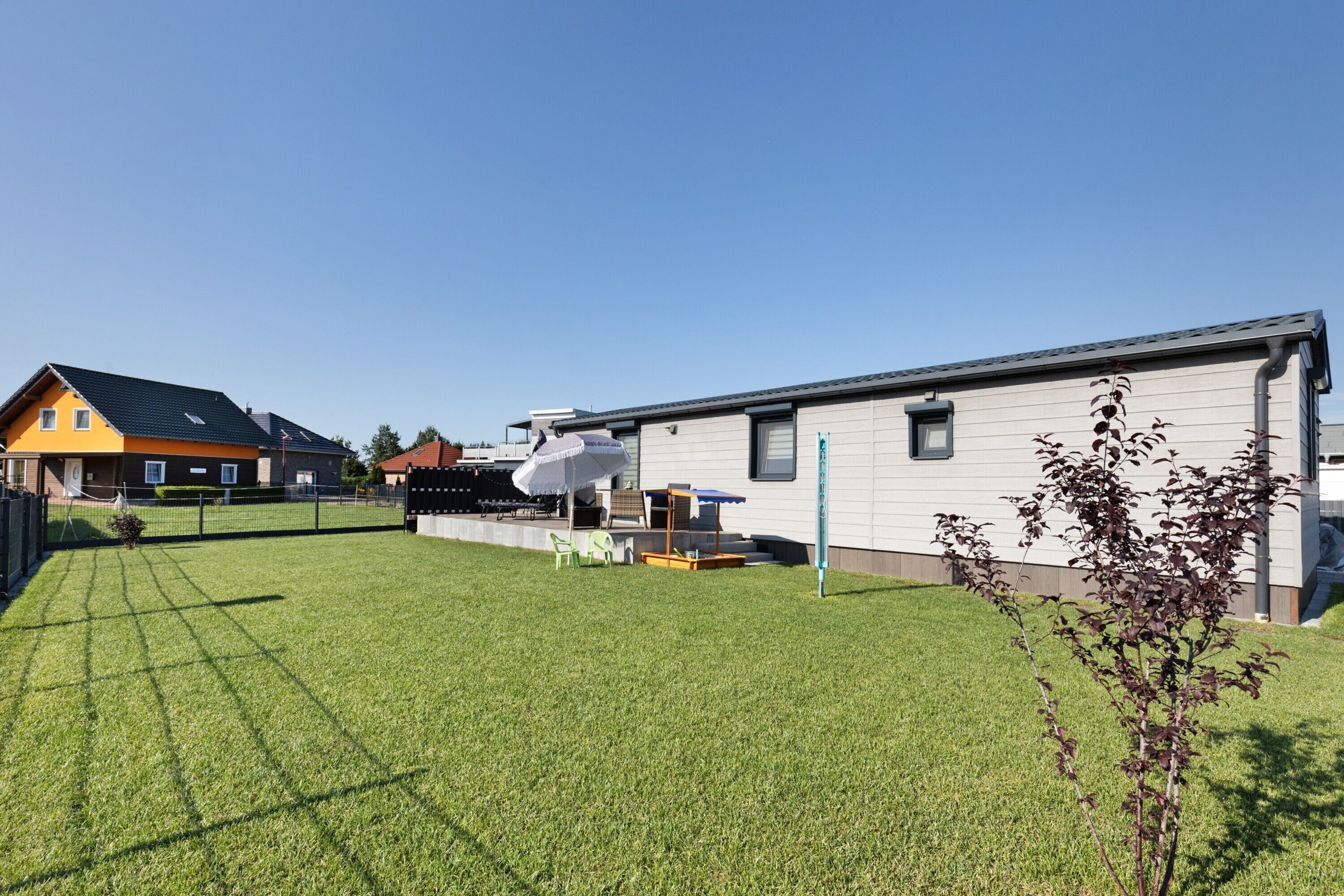 A residential area with a well-maintained lawn, a small play area, and a house with a grey exterior and a blue roof.