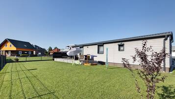 A residential area with a well-maintained lawn, a small play area, and a house with a grey exterior and a blue roof.