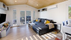 A modern living room with a sofa, TV, and a dining area. - Holiday Home 'Madera Concordiasee' with Wi-Fi and Air Conditioning (Seeland)