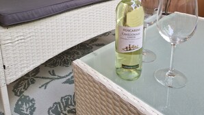 A wicker sofa with cushions, a glass table with a bottle of wine and a glass, and a potted plant. - Apartment Eschenweg incl. balcony with garden view, bed linen and towels (Bad Harzburg)