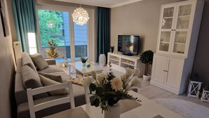 A modern living room with a sofa, dining table, TV, and a cabinet. - Apartment Eschenweg incl. balcony with garden view, bed linen and towels (Bad Harzburg)