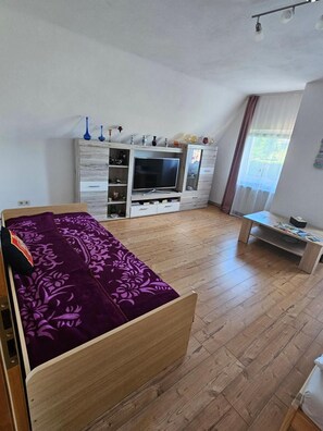 A bedroom with a bed, a TV, a dresser, and a window.