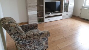A living room with a sofa, a TV on a wooden entertainment unit, and a window. - Apartment 'Ferienwohnung Peter' (Rudolstadt)