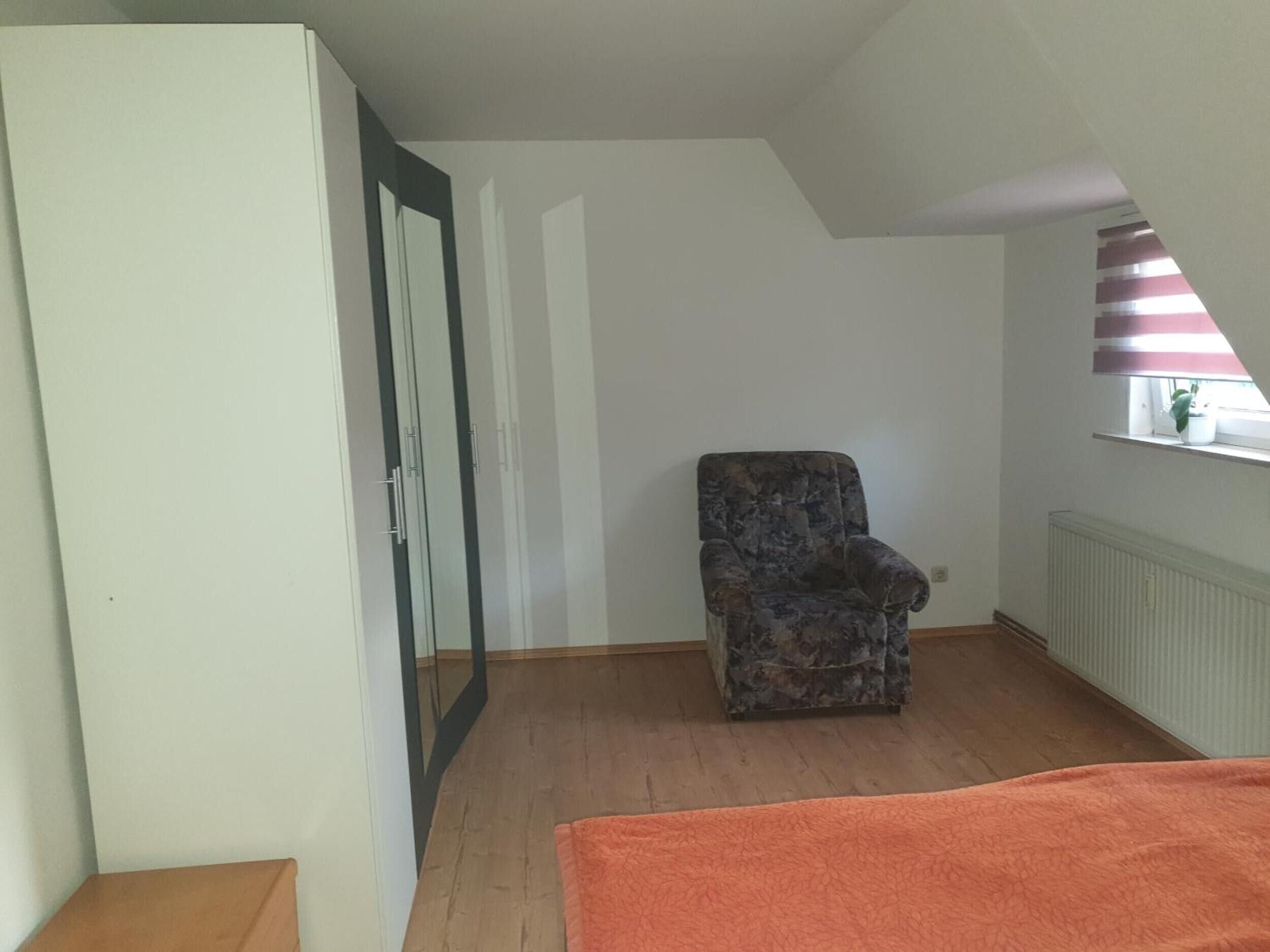 Une pièce avec un plancher en bois, une chaise, un lit et un radiateur.
