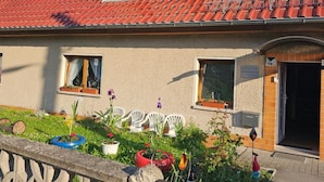 A two-story house with a red-tiled roof, a small balcony, and a front garden with potted plants and outdoor furniture. - Apartment 'Ferienwohnung Peter' (Rudolstadt)