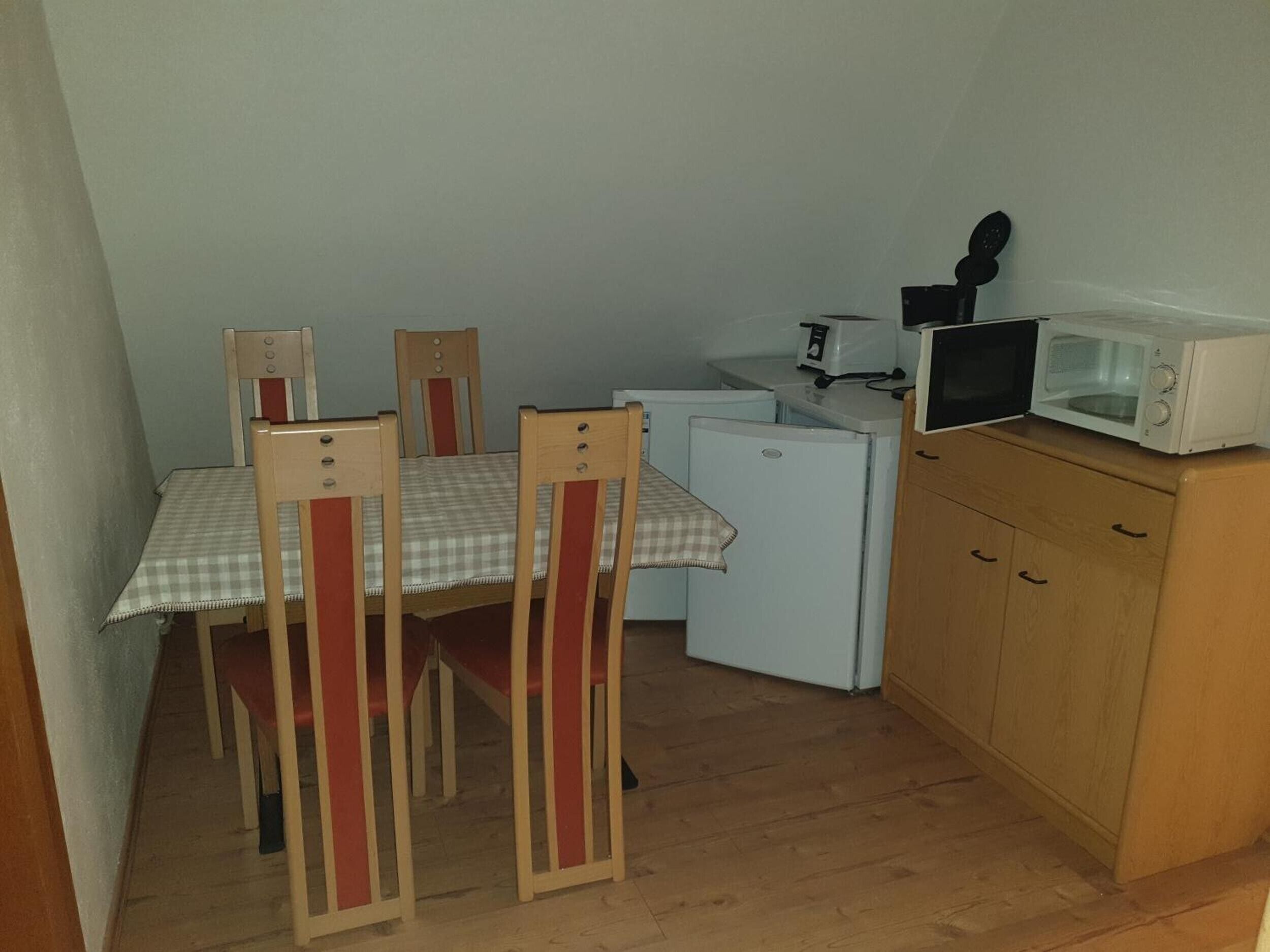A compact kitchen with a dining table, chairs, a refrigerator, a microwave, and a small countertop with a toaster.