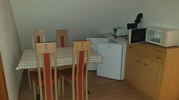 A compact kitchen with a dining table, chairs, a refrigerator, a microwave, and a small countertop with a toaster.