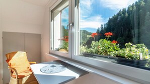 A room with a wicker chair, a small table, and a window overlooking a garden with red flowers. - Apartment 'Ferienwohnung 1 Talblick' with Mountain View, Shared Terrace and Wi-Fi (Oppenau)