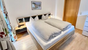 A bedroom with a bed, a nightstand, a lamp, a wooden headboard, a door, and a wall-mounted picture. - Apartment 'Ferienwohnung 1 Talblick' with Mountain View, Shared Terrace and Wi-Fi (Oppenau)