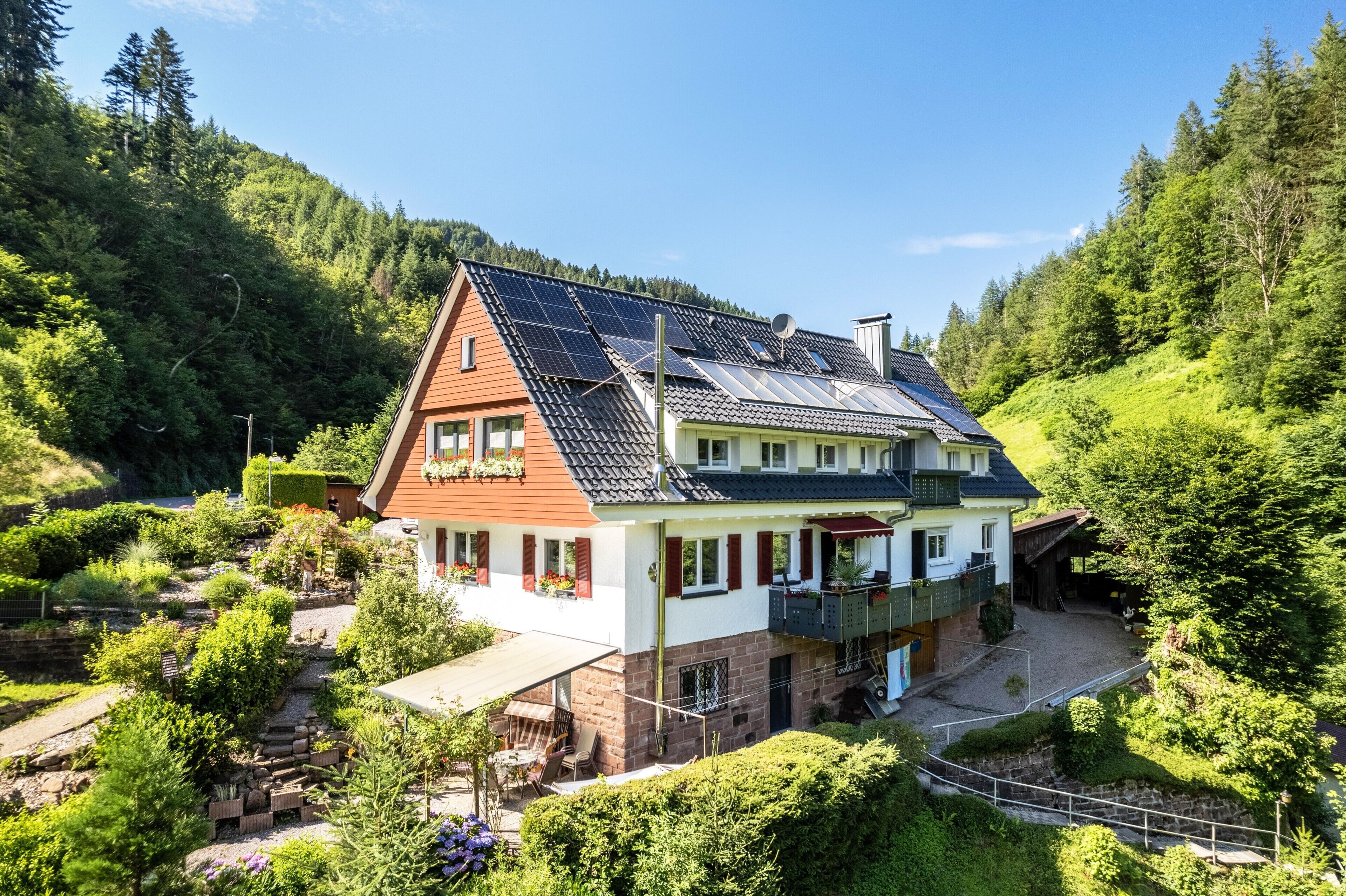 Uma casa com telhado inclinado, painéis solares e um jardim.