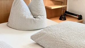 Een keurig opgemaakt slaapkamer met een bed, kussens, een bedlampje en een stekkerdoos.