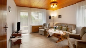 Ein Wohnzimmer mit Holzboden, einer Couch, einem Couchtisch und einem Fernseher.