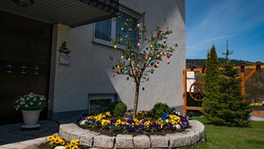 Ein Gebäude mit einem Baum, der mit bunten Verzierungen geschmückt ist, einem Blumenbeet mit verschiedenen Blumen und einer kleinen Weihnachtstanne.