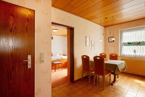 Une pièce avec une porte en bois, une table à manger avec des chaises, un lit et une fenêtre avec des rideaux.