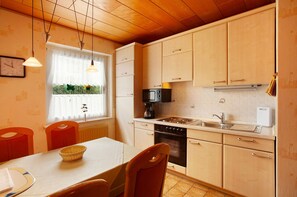 Une cuisine avec des meubles en bois, une cuisinière, un four à micro-ondes et une fenêtre donnant sur un paysage verdoyant.