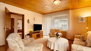 A living room with a television, two armchairs, a coffee table, and a window with blinds.