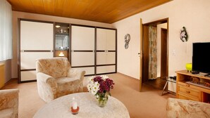 A traditional Japanese-style room with tatami flooring, a low wooden table, a sofa, a TV, and a sliding door leading to another room.