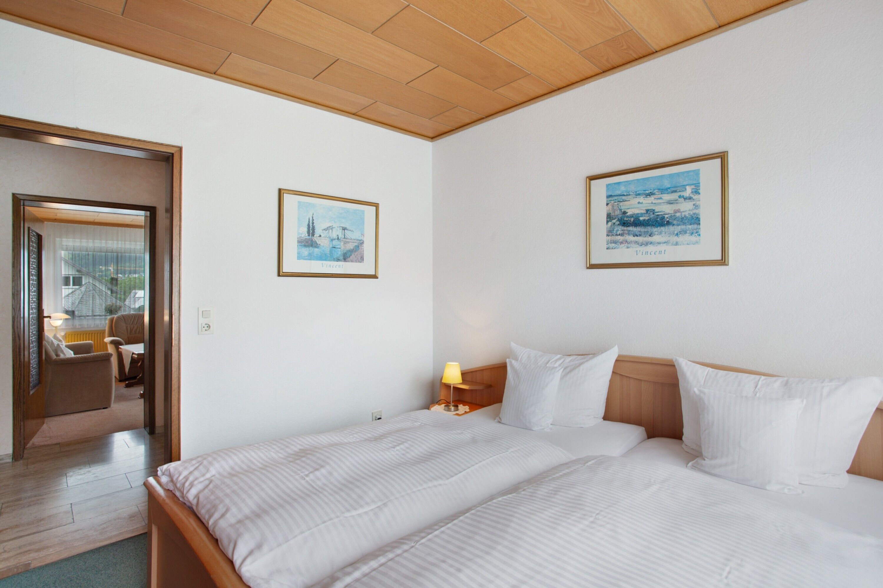 A hotel room with a bed, a nightstand, a lamp, and two framed pictures on the wall.