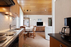 A kitchen with wooden cabinets, a stove, a sink, and a dining area with chairs and a table.