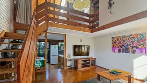 Amplia sala de estar con una escalera de madera, un televisor y un cuadro de colores en la pared.