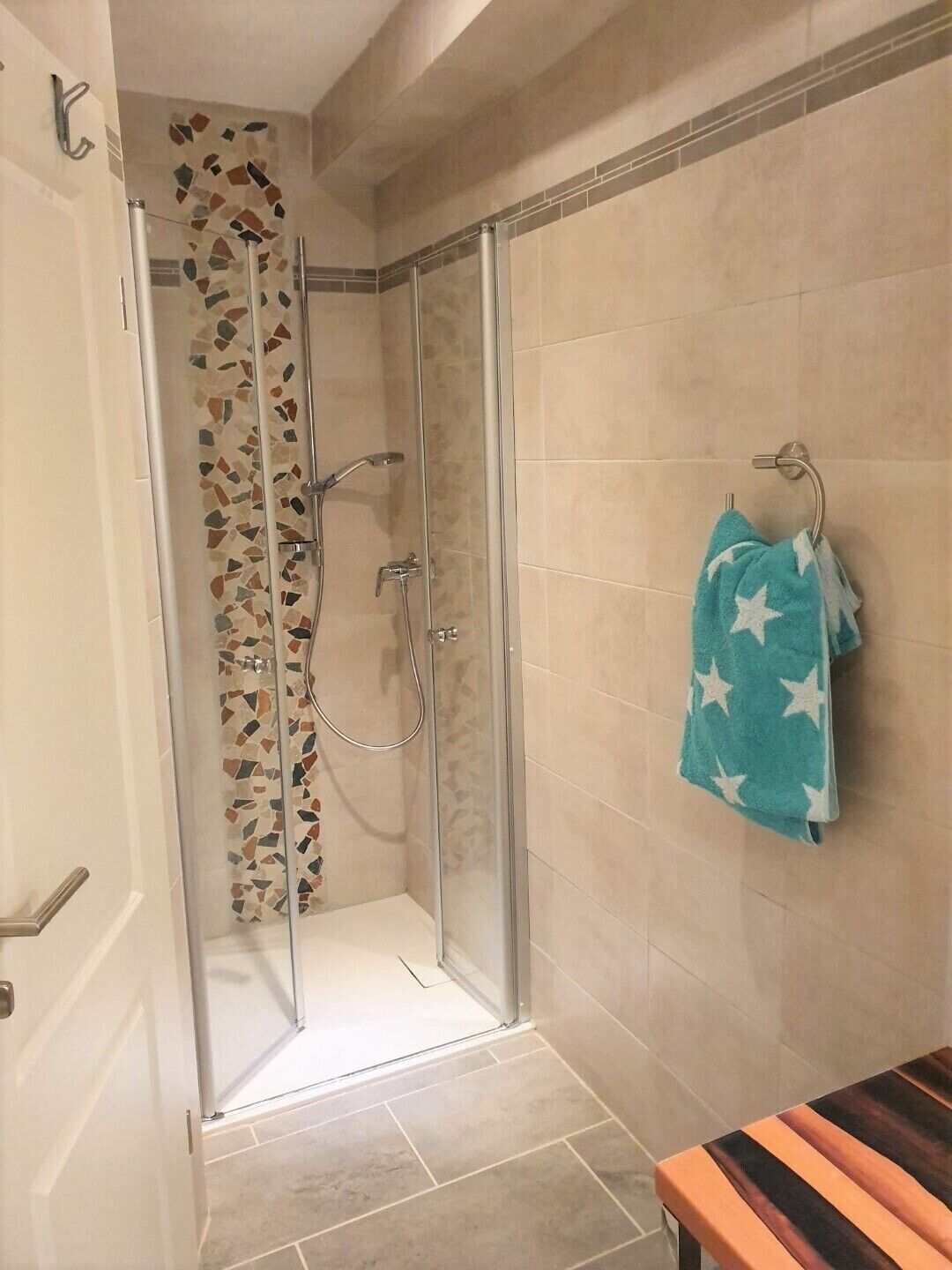 A glass-enclosed shower with a mosaic tile wall, a towel rack with a towel, and a wooden bench.