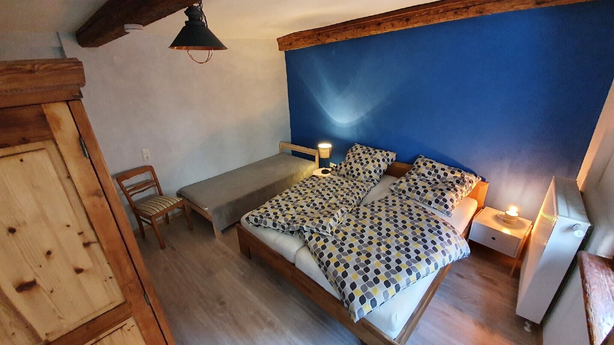 Een slaapkamer met een bed, twee nachtkastjes, een stoel, een houten garderobe en een hanglamp.