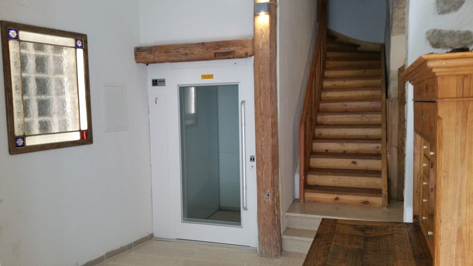 A room with a wooden staircase, a door with a glass panel, and a wooden cabinet.