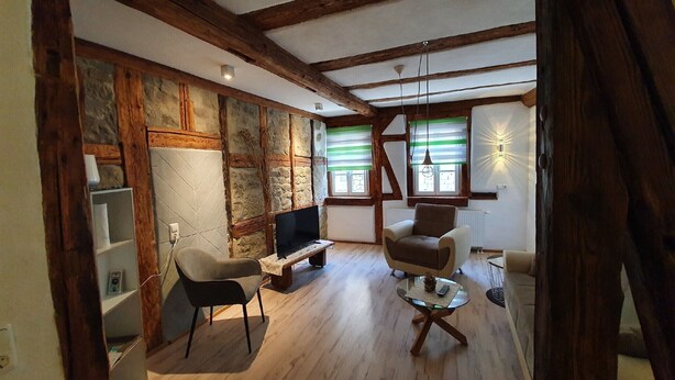 A room with exposed wooden beams, a stone wall, a television, and a sofa.
