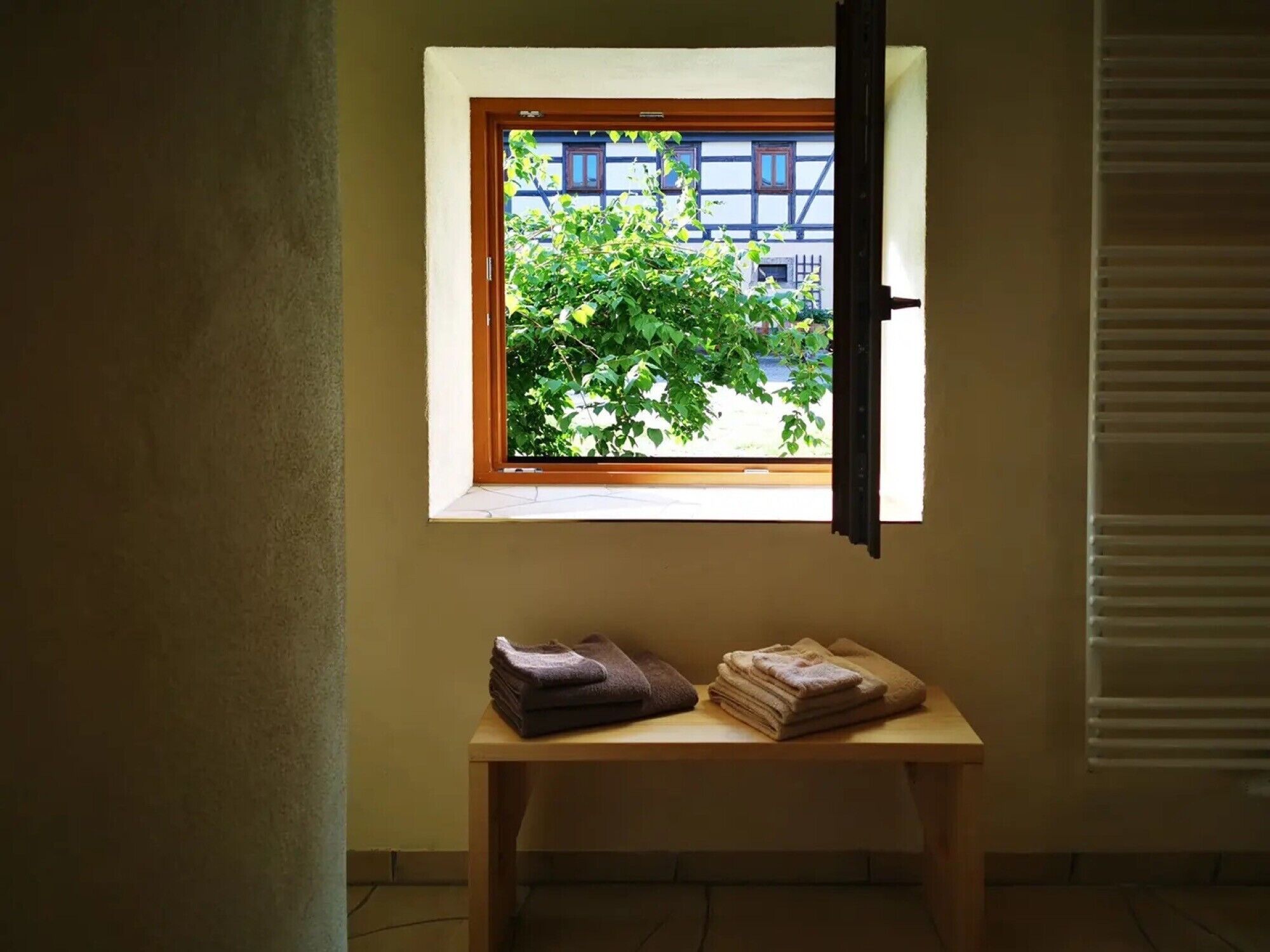 A room with a window, a small table with folded towels, and a view of a building outside.