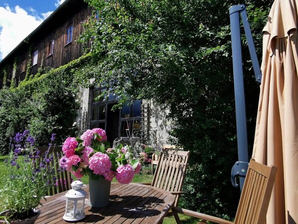 A wooden deck with a table, chairs, a lantern, and a potted plant with pink flowers.