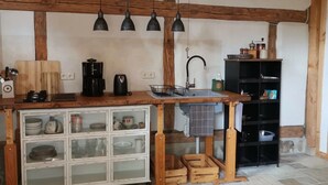 Una cocina rústica con vigas de madera a la vista, encimera de madera, mueble empotrado con puertas de cristal, cafetera y lámparas colgantes.