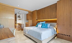 Une chambre moderne avec un grand lit, une tête de lit en bois et un coin repas comprenant une table et des chaises en bois.