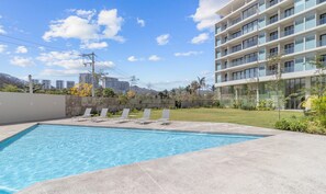 Une piscine avec des chaises longues, une pelouse et un bâtiment moderne doté de nombreux balcons.