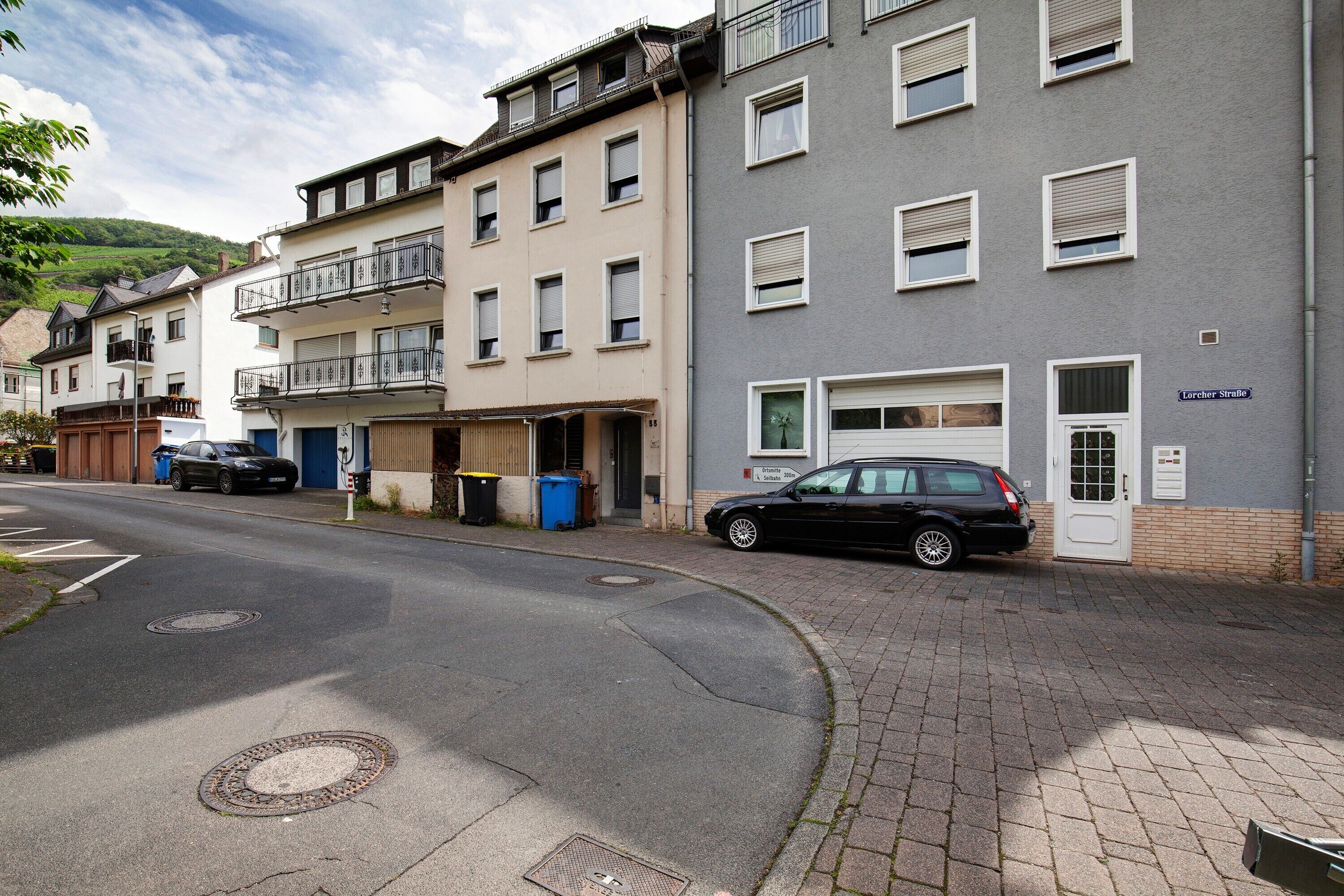Une rue bordée d’immeubles d’habitation, une voiture garée et un regard d’égout.
