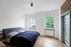 A bedroom with a bed, two windows, a radiator, and a door.