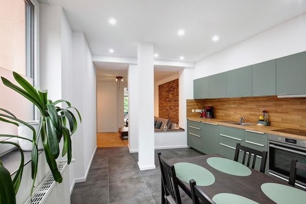 A modern kitchen with green cabinets, a wooden countertop, and a dining area with a table and chairs.