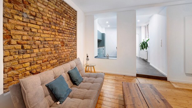 Een moderne woonkamer met een bakstenen muur, een bank met kussens, een klein rond tafeltje en een houten vloer.