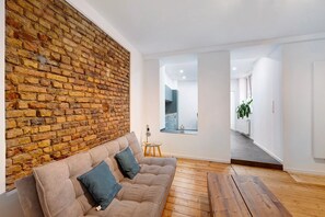 A modern living room with a brick wall, a sofa with cushions, a small round table, and a wooden floor.