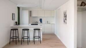 A modern kitchen with white cabinets, a central island with stools, and a sink. - Beach Gardens 46 by Daniel&Jacob's (København)