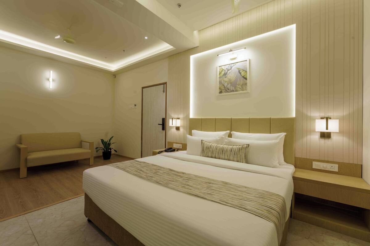 Une chambre d’hôtel avec un grand lit, des tables de chevet, un canapé et une œuvre d’art accrochée au mur.
