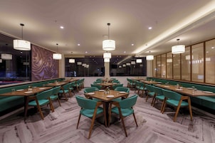 Un restaurante con largas mesas de madera, sillas color turquesa e iluminación colgante.