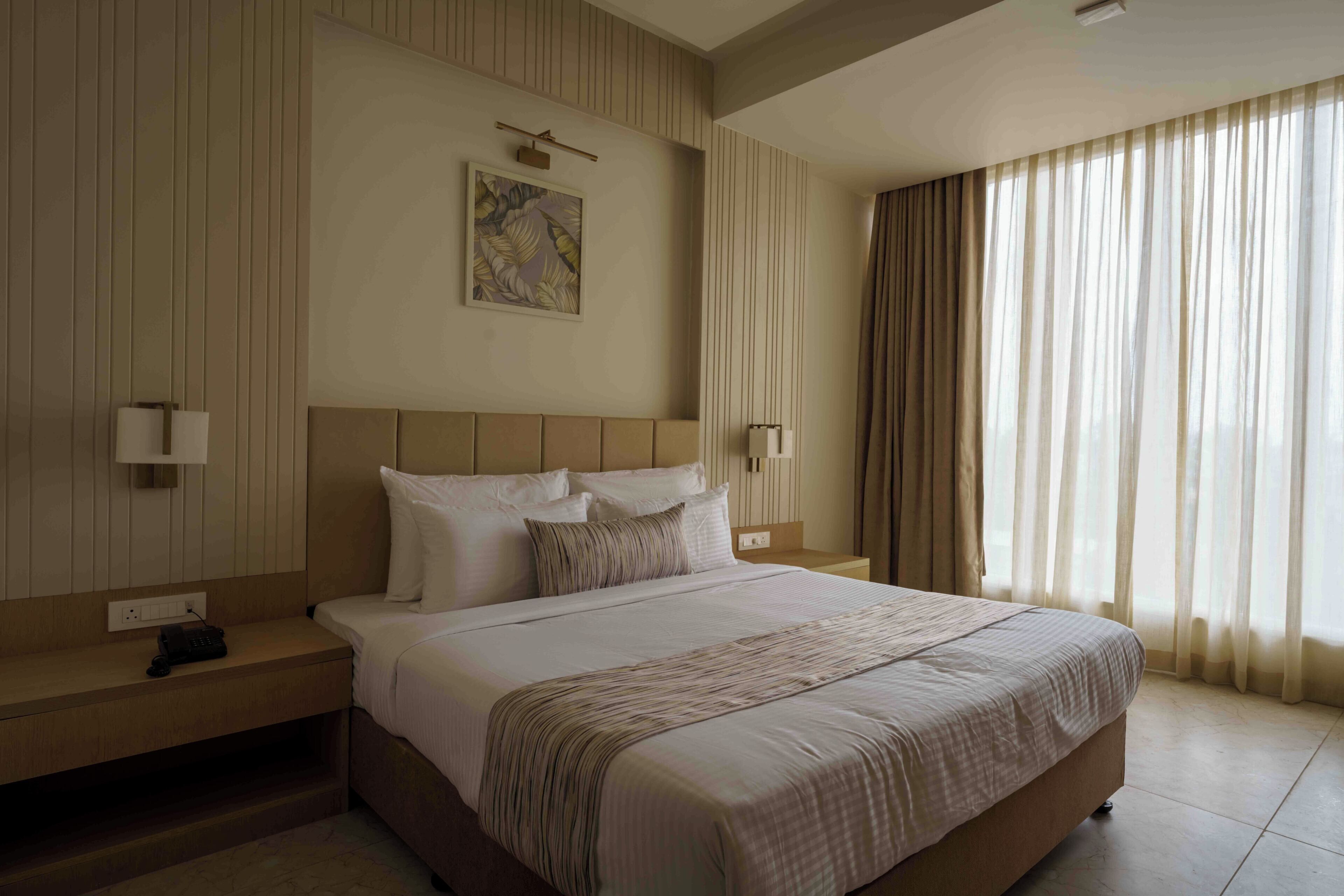 A hotel room with a large bed, two bedside tables, a wall-mounted lamp, and a window with curtains.